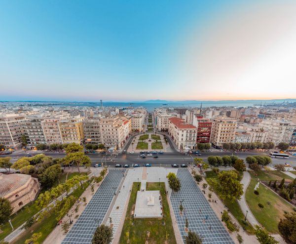Aerial view of a Greek city square with buildings and sea in the background.